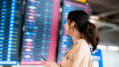 Eine Frau am Flughafen mit Noise Canceling Kopfhörern im Ohr - Foto: Amazon/PR