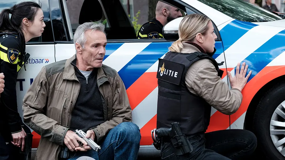 Der Amsterdam-Krimi: Der falsche Tote Charaktere verstecken sich hinter Polizeiwagen.