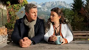 Der Bergdoktor und eine Frau sitzen draußen an einem Tisch. - Foto: SRF/ZDF/Erika Hauri