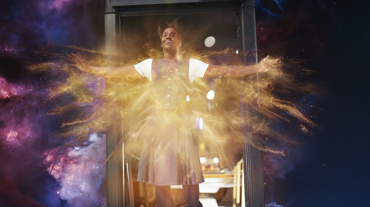 Der Doktor nahm im Finale von Staffel 2 eine unerwartete, neue Form an. Der Doktor steht im Türrahmen der TARDIS, die im Weltall schwebt. Er lächelt und breitet die Arme aus, sein Körper ist umgeben von goldenem Licht.