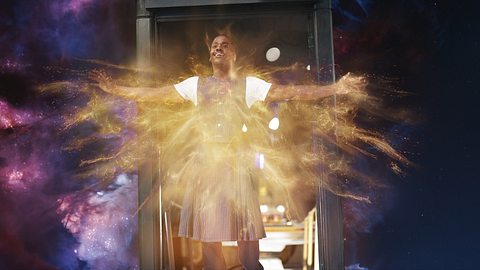 Der Doktor steht im Türrahmen der TARDIS, die im Weltall schwebt. Er lächelt und breitet die Arme aus, sein Körper ist umgeben von goldenem Licht. - Foto: James Pardon/BBC Studios/Bad Wolf
