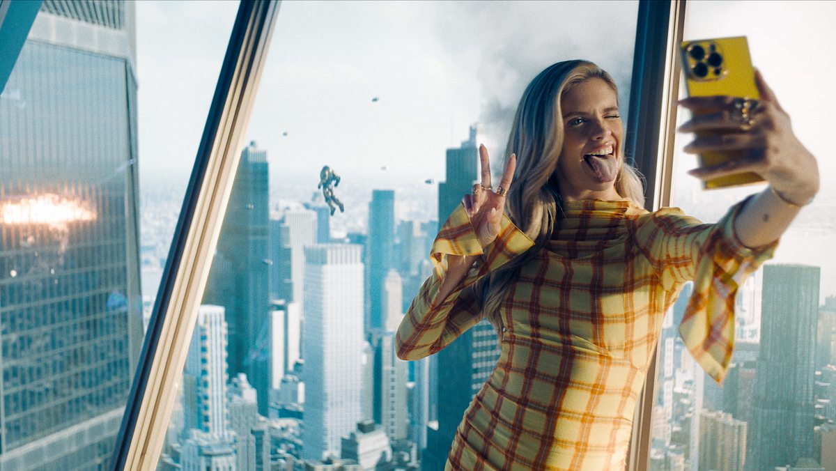 Eve Teschmacher macht ein Selfie vor einem Fenster, hinter ihr findet ein Kampf im Himmel statt.