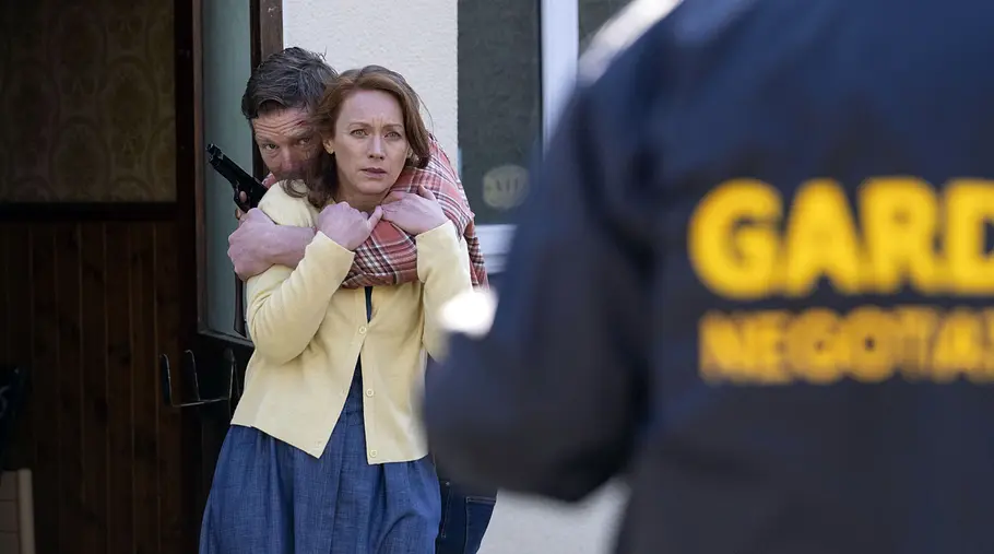 Ronan hat einen Arm und seine noch Ehefrau Grace geschlungen und hält eine Pistole in der anderen.