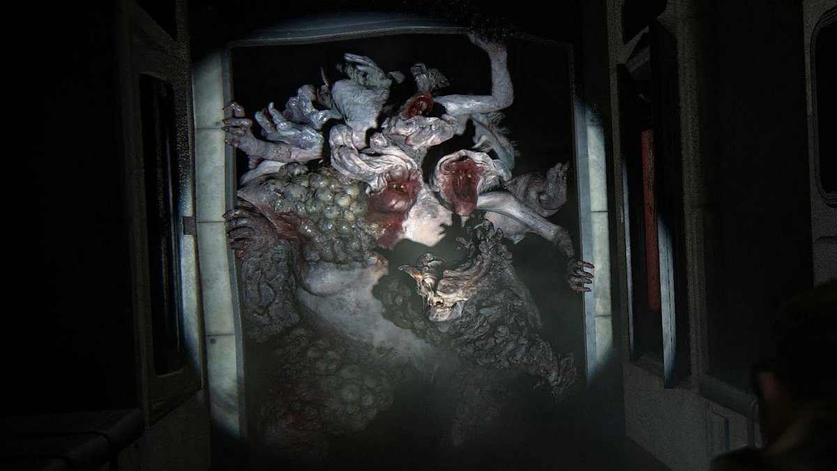 Der Rattenkönig überrascht Abby in „The Last of Us – Part II“. Eine aus mehreren Zombies bestehende Kreatur bricht durch eine Tür und wird von einer Taschenlampe beleuchtet.