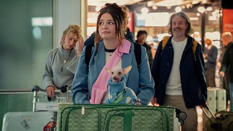 Jess mit Koffern und Hund am Flughafen. Sie schaut skeptisch zur Seite. - Foto: © 2024 Netflix, Inc.