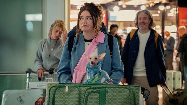 Jess mit Koffern und Hund am Flughafen. Sie schaut skeptisch zur Seite. - Foto: © 2024 Netflix, Inc.