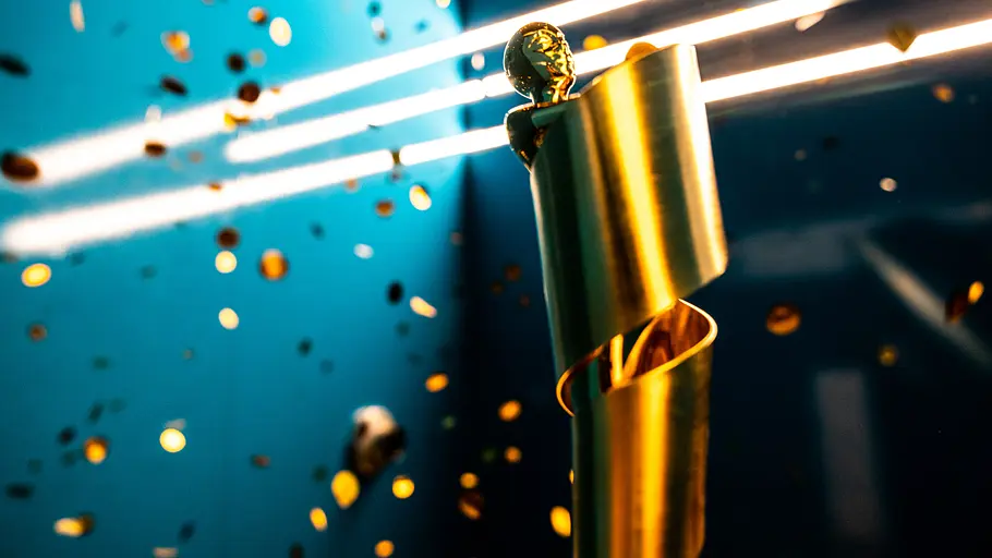 Filmpreis Lola Goldene Lola-Trophäe des Deutschen Filmpreises vor blauem Hintergrund, umgeben von herabfallendem Konfetti und Lichtstreifen.