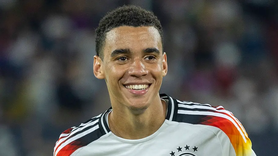 Jamal Musiala steht auf dem Feld und lächelt.