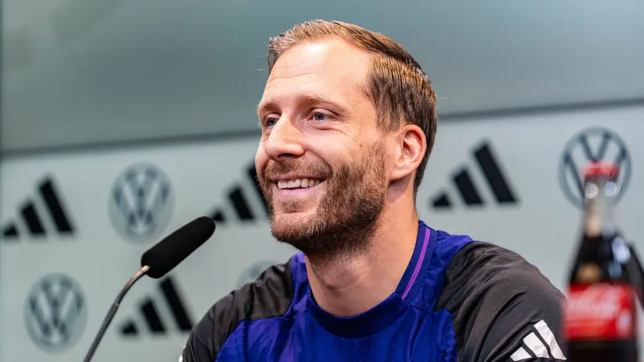 Oliver Baumann sitzt in einer Pressekonferenz und lächelt.