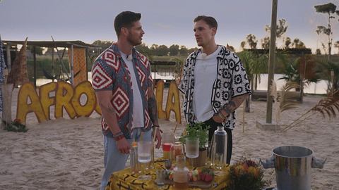 Martin Braun und Felix Stein stehen gemeinsam am Strand, vor ihnen stehen einige Getränke - Foto: RTL