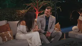Tim sitzt mit einer Kandidatin, die der Kamera den Rücken zukehrt, auf einem Day-Sofa und redet. Er lacht sie an. - Foto: RTL