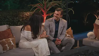 Tim sitzt mit einer Kandidatin, die der Kamera den Rücken zukehrt, auf einem Day-Sofa und redet. Er lacht sie an. - Foto: RTL