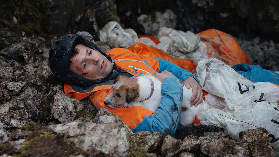 „Die Bergretter“ Staffel 18: Steve verunglückt bei Rettungsversuch von Hund Monti Steve liegt nach einem Unfall verletzt in felsigem Gelände und hält Hund Monti im Arm.