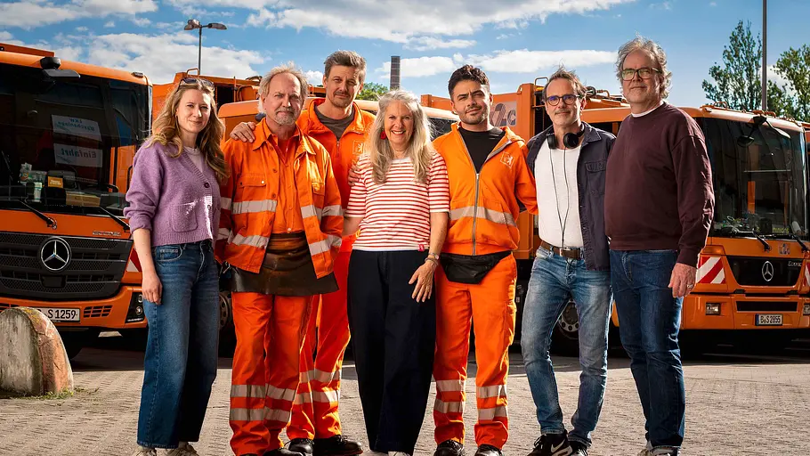 Die Drei von der Müllabfuhr Der Cast und die Crew von „Die Drei von der Müllabfuhr“ stehen vor mehreren Müllwagen.