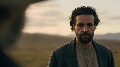 Christopher Abbott als Adam Trask steht mit Bart und dunklem Mantel vor einer kargen Landschaft und blickt ernst nach links. - Foto: © 2026 Netflix, Inc.