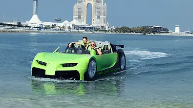Robert und Shania Geiss fahren mit einem neongrünen Amphibien-Sportwagen über das Wasser vor der Skyline von Abu Dhabi. - Foto: RTLZWEI