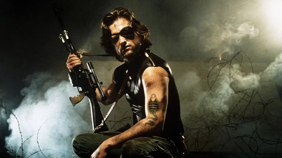 Die Klapperschlange Kurt Russell steht als Snake Plissken für „Die Klapperschlange“ vor Stacheldraht im Nebel. Er hat eine Schusswaffe in der Hand.
