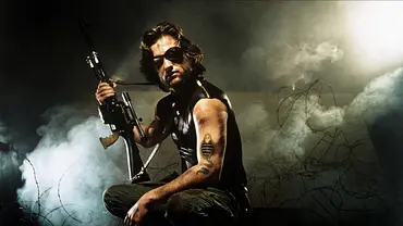 Kurt Russell posiert als Snake Plissken mit einer Schusswaffe vor Stacheldraht im Nebel. - Foto:  IMAGO / Allstar