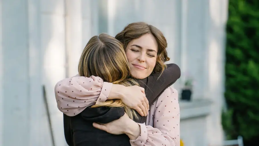 DIE LANDARZTPRAXIS-Vorschau FOLGE 86 Montag 26. Oktober Zwei Frauen umarmen sich vor einer hellen Hauswand. Die Frau in der rosa gepunkteten Bluse hat die Augen geschlossen.
