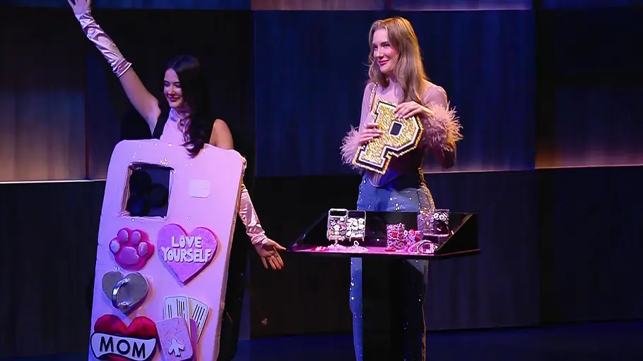 Die Löwen würden sich wohl keine POP CHARMS aufs Smartphone kleben. Kerstin Raibold steht rechts mit einem glitzernden P neben einer Frau im rosa Handyhüllen-Kostüm, die einen Arm hebt.