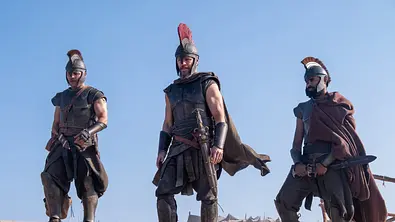 Jimmy Gonzales, Matt Damon und Himesh Patel stehen in Rüstungen an einem Strand. - Foto: © Universal Studios. All Rights Reserved.