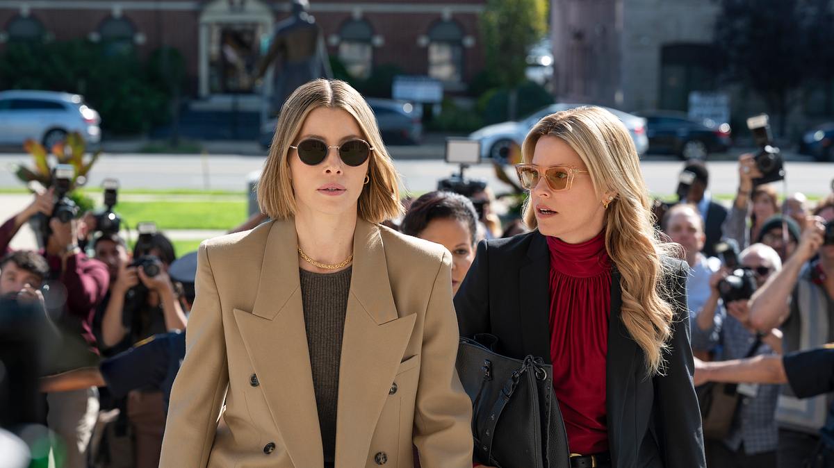 Staffel 1 bietet ein rundes Ende - doch die Geschichte könnte weitergehen. Elizabeth Banks als Nicky und Jessica Biel als Chloe gehen nach vorne. Nicky schaut geschockt zu Chloe, hinter ihnen stehen Reporter:innen mit Kameras.