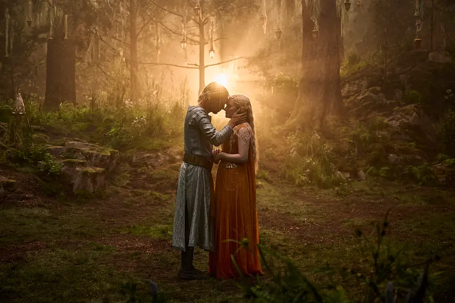 Celeborn kehrt zu Galadriel zurück Celeborn hält Galadriels Gesicht zärtlich in den Händen. Sie stehen in einem Wald mit hängenden Laternen im goldenen Licht.