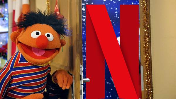Ernie lacht in die Kamera und steht neben einer offenen Tür. Vor der Tür steht das Netflix-Logo. - Foto: © NDR/Studio Hamburg/Boris Laewen/KiKA/Netflix