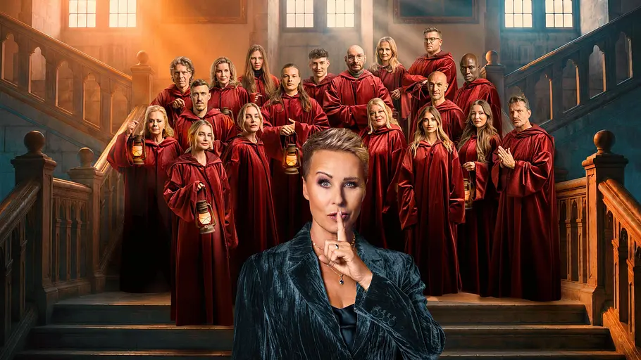 Bei Die Verräter mussten wieder zwei Promis gehen. Sonja Zietlow hält einen Finger vor dem Mund, im Hintergrund sind die Stars zu sehen.