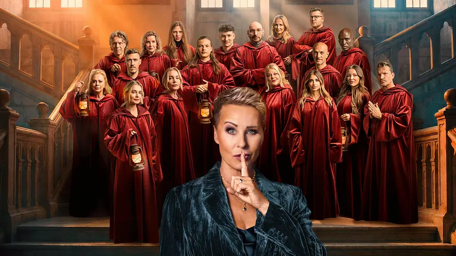 Sonja Zietlow hat sich ihre Verräter ausgesucht. Sonja Zietlow hält einen Finger vor dem Mund, im Hintergrund sind die Stars zu sehen.