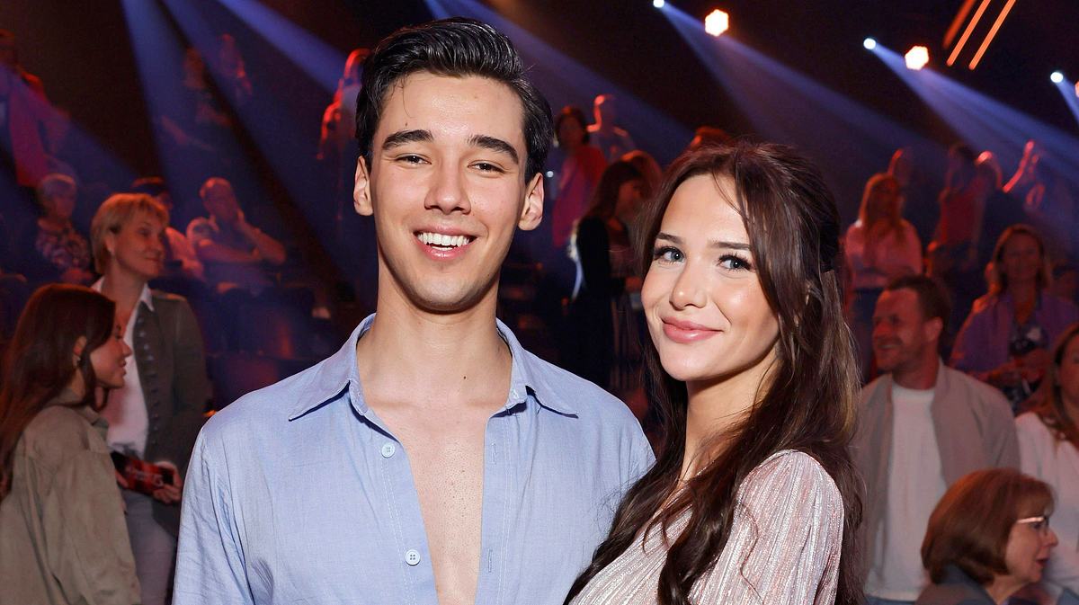 Diego Pooth und seine Freundin Louisa Büscher. Diego Pooth und seine Freundin Louisa Büscher lächeln in die Kamera. Das blaue Hemd von Diego ist unanständig weit aufgeknöpft.