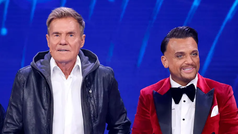 Dieter Bohlen und Menowin Fröhlich Dieter Bohlen steht mit ernstem Blick und Lederjacke neben einem lächelnden Menowin Fröhlich.