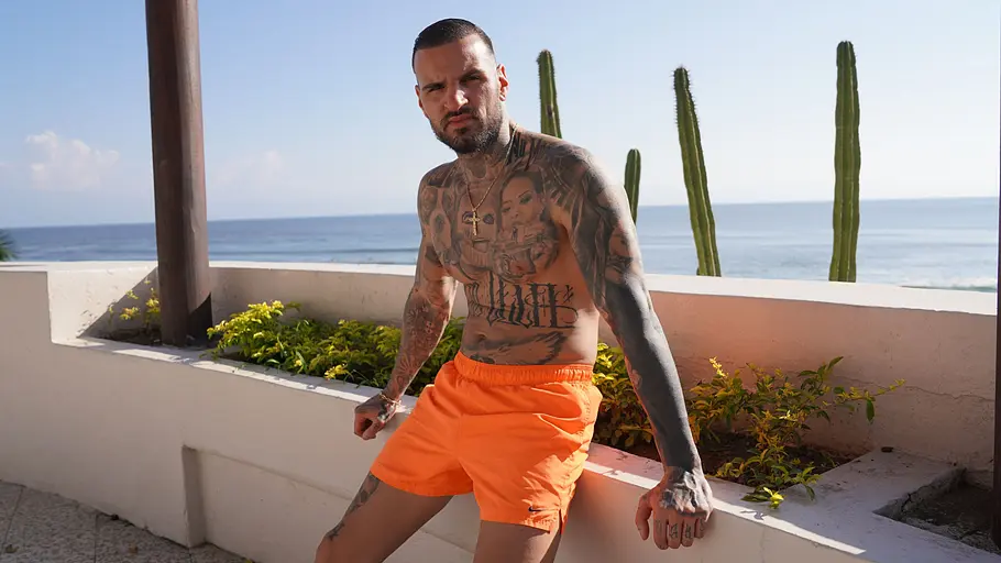 Diogo sitzt in orangener Badehose auf einer Mauer. Im Hintergrund sieht man Meer.
