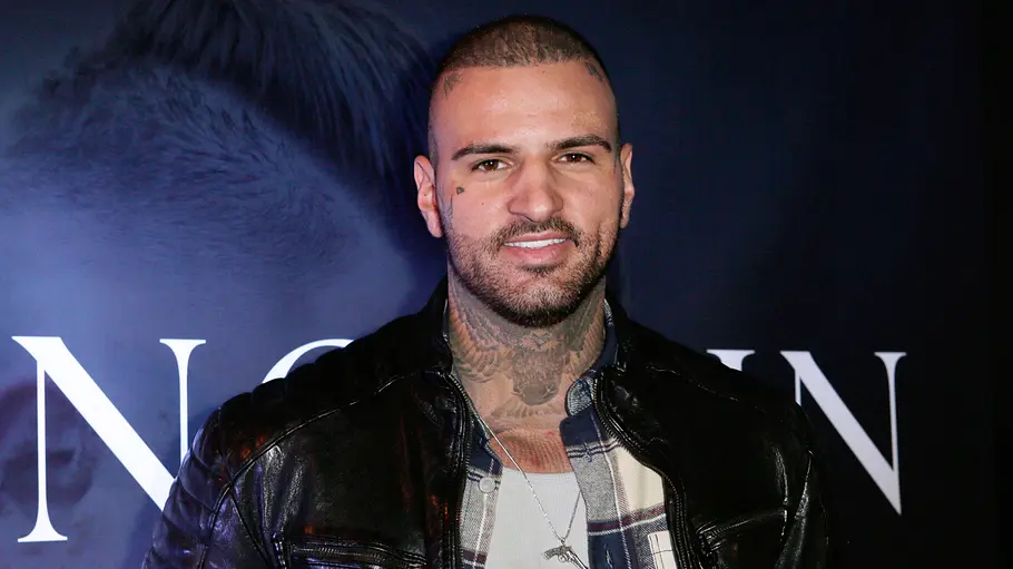 Diogo Sangre Diogo Sangre trägt eine schwarze Lederjacke über einem karierten Hemd. An Hals und Brust sind Tattoos sichtbar.