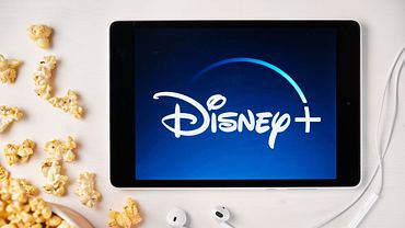 Ein Tablet, auf dem das Disney+-Logo zu sehen ist. Daneben liegt Popcorn. - Foto: IMAGO / Dreamstime