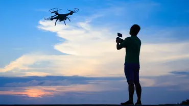Die Silhouette eines Mannes, der eine Drohne bei strahlendem Himmel fliegen lässt. - Foto: Canva