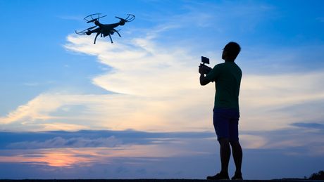 Die Silhouette eines Mannes, der eine Drohne bei strahlendem Himmel fliegen lässt. - Foto: Canva