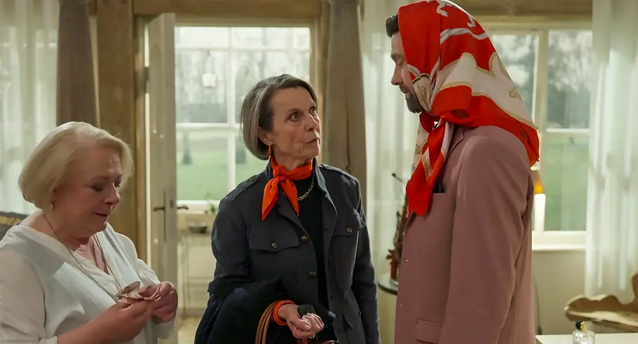 Gisela, Victoria und Julius stehen in einem hellen Raum. Julius trägt ein rotes Kopftuch und ein rosafarbenes Sakko.