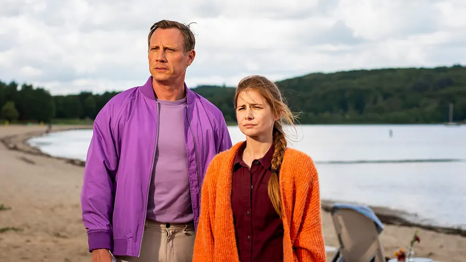 Dr. Nice und Charlie am Strand. Am Sandstrand stehen Dr. Nice (Patrick Kalupa) und Charlie (Josefine Preuß) nebeneinander. Beide schauen mit traurigen Blick seitlich nach vorne.