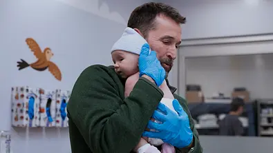 Dr. Robby hält ein Baby. - Foto: Warrick Page/HBO Max