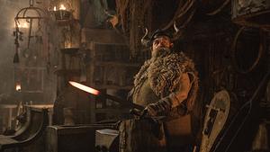Nick Frost steht als der blonde, sowie bärtige Wikinger Grobian in grünlicher Wikinger-Montur vor einem Amboss und hat ein heißes Stück Metall in der Hand. - Foto:  IMAGO / Cinema Publishers Collection