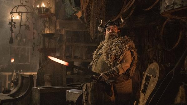 Nick Frost steht als der blonde, sowie bärtige Wikinger Grobian in grünlicher Wikinger-Montur vor einem Amboss und hat ein heißes Stück Metall in der Hand. - Foto:  IMAGO / Cinema Publishers Collection