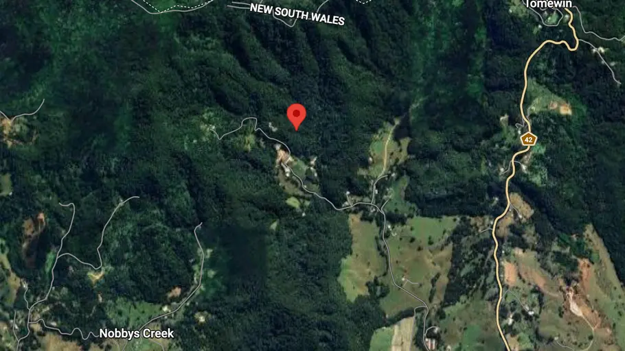 Der Drehort vom Dschungelcamp Satellitenbild von dicht bewaldetem Gebiet an der Grenze von Queensland und New South Wales, Australien, mit markiertem Standort nahe Tomewin.