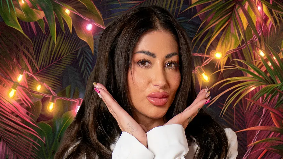 Reality-TV-Star Bellydah posiert für ein Promobild von „Dschungel Divas“ in roter Spitzenwäsche und einem weißen Blazer vor einer tropischen Kulisse mit Lichterketten und großen Palmenblättern. Mit beiden Händen an ihrem Gesicht blickt sie direkt in die Kamera.