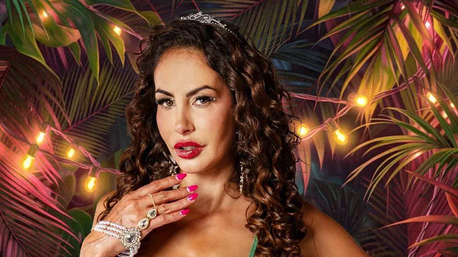 Janina Youssefian Janina Youssefian im grünen, figurbetonten Kleid mit langen Locken vor tropischer Dschungelkulisse und bunten Lichterketten.