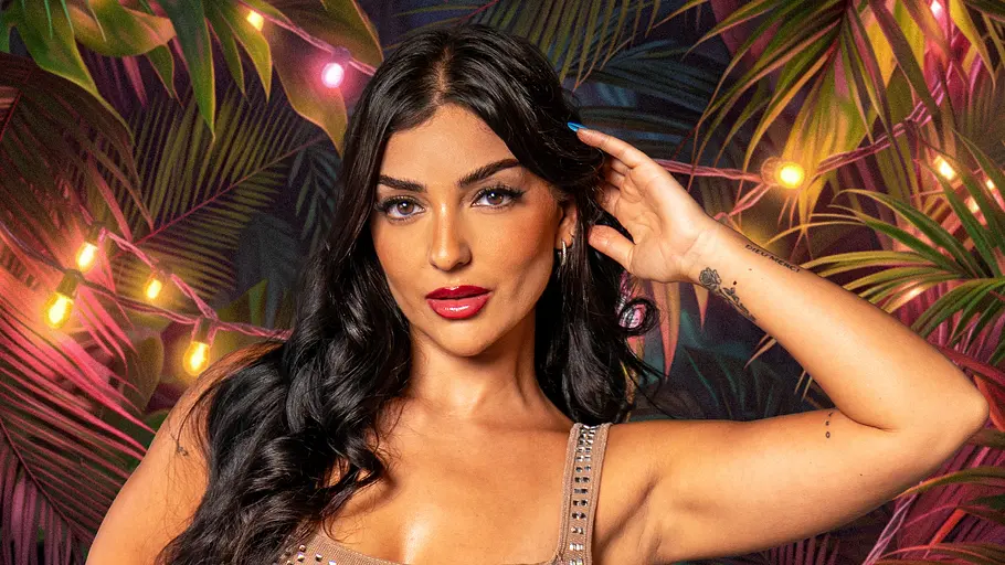 Reality-TV-Star Jennifer Iglesias posiert für ein Promobild von „Dschungel Divas“ in einem glitzernden, eng anliegenden Kleid vor einer tropischen Kulisse mit Palmenblättern und bunten Lichterketten. Sie blickt selbstbewusst in die Kamera und hat eine Hand an ihre Haare gelegt.