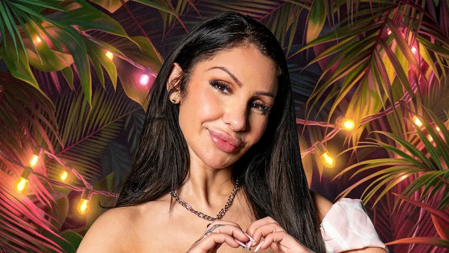 Reality-TV-Star Pinar Sevim posiert für ein Promobild von „Dschungel Divas“ in einem rosafarbenen Off-Shoulder-Top und Jeansrock vor einer tropischen Kulisse mit Lichterketten und großen Palmenblättern. Mit den Händen formt sie ein Herz und lächelt in die Kamera.