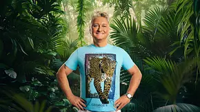 Hubert Fella steht lächelnd im Dschungelcamp-Promo-Setting vor dichtem, tropischem Blätterwald. Er trägt ein türkisfarbenes T-Shirt mit Leopardenmotiv und weiße Hose, die Hände selbstbewusst in die Hüften gestützt. - Foto: RTL / Hintergrund KI-generiert Hubert Fella steht lächelnd im Dschungelcamp-Promo-Setting vor dichtem, tropischem Blätterwald. Er trägt ein türkisfarbenes T-Shirt mit Leopardenmotiv und weiße Hose, die Hände selbstbewusst in die Hüften gestützt. - Foto: RTL / Hintergrund KI-generiert
