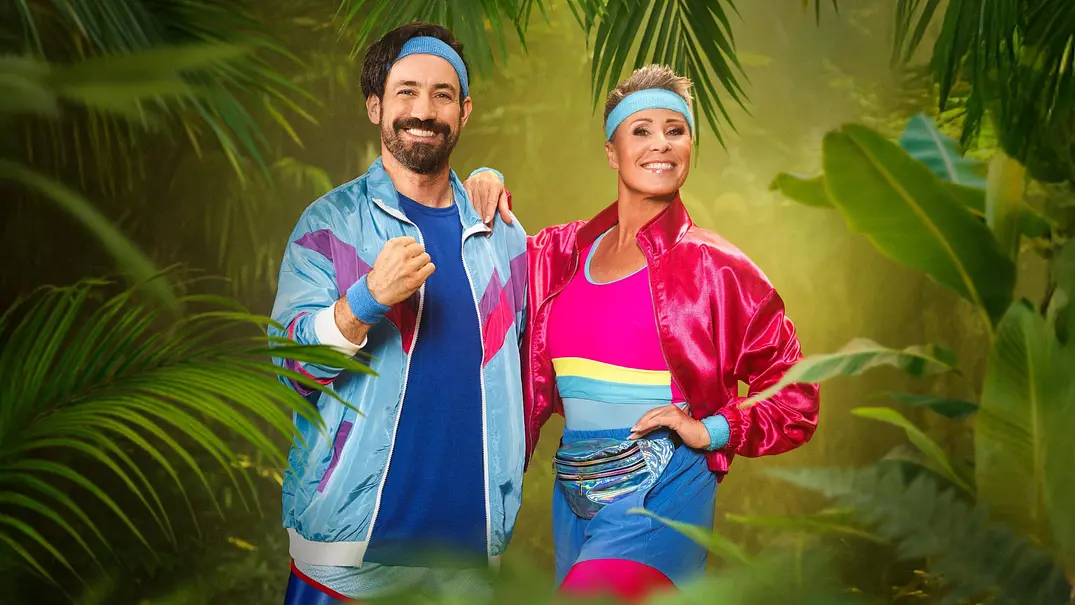 Jan Köppen und Sonja Zietlow stehen im Sportanzug im Dschungel-Setting und lachen - Foto: RTL / Pascal Bünning Jan Köppen und Sonja Zietlow stehen im Sportanzug im Dschungel-Setting und lachen - Foto: RTL / Pascal Bünning