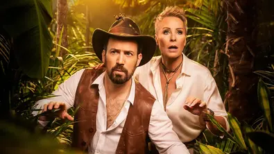 Jan Köppen mit Hut und Bart und Sonja Zietlow mit kurzem Haar stehen in Abenteurerkleidung im dichten Dschungel; beide schauen gespannt und leicht besorgt nach vorne, umgeben von tropischen Pflanzen. - Foto: RTL